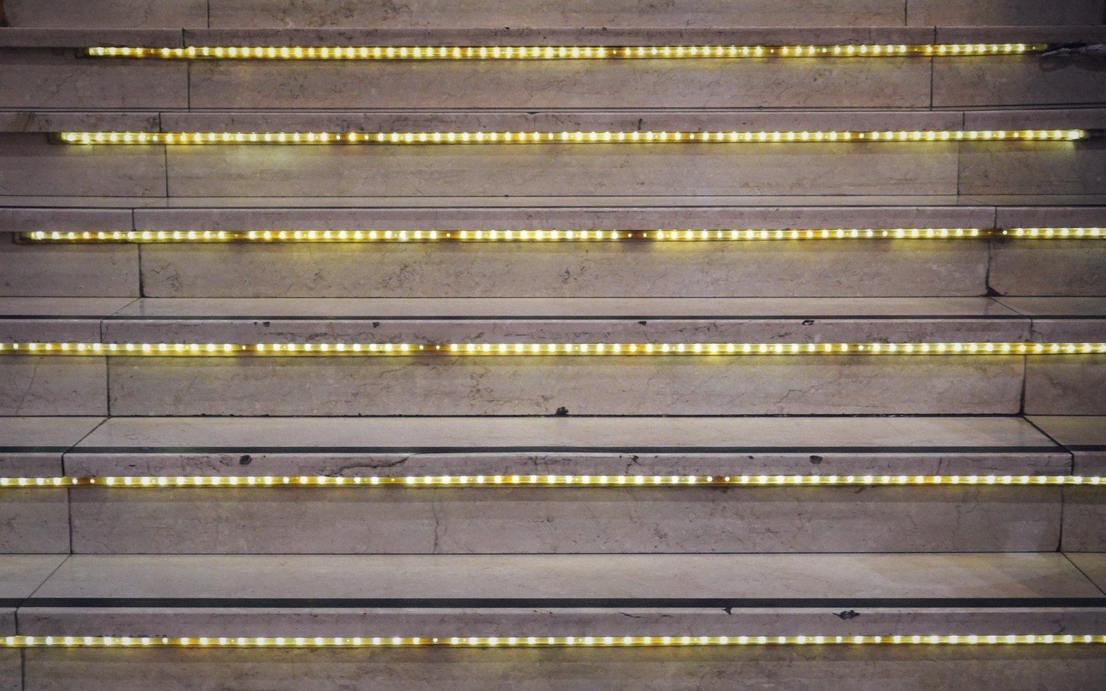 Marble stairs lined with glowing yellow LED strip lights along each step's edge